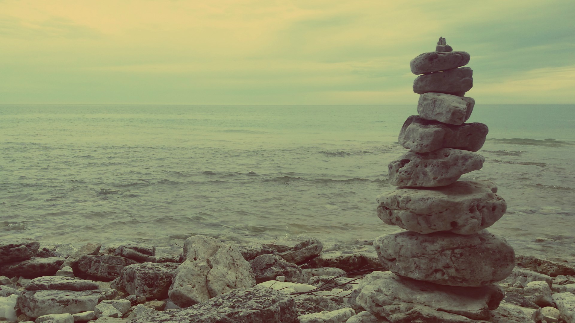Stacked stones on a rocky shore by the sea HD Wallpaper