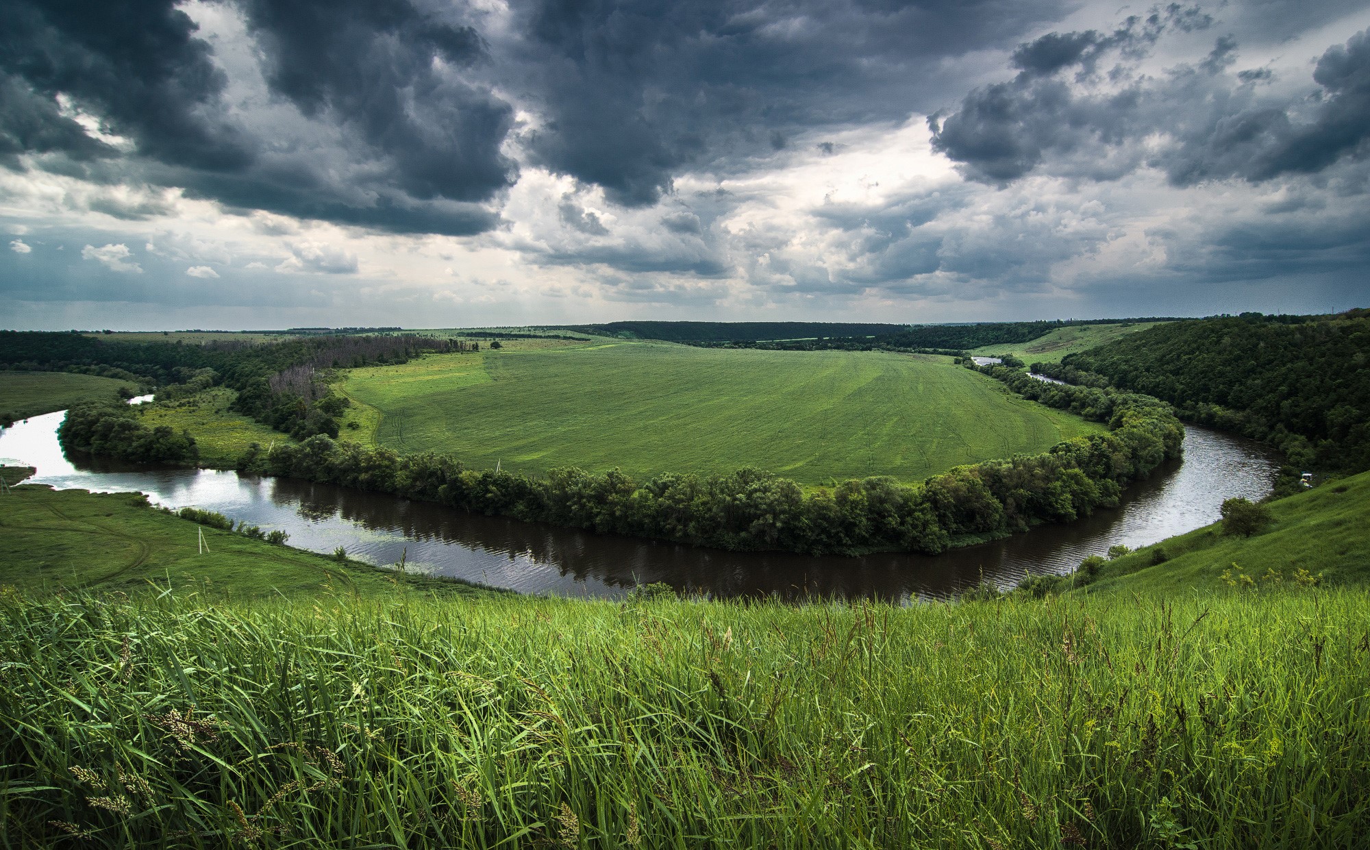 River winding through green fields under stormy sky HD Wallpaper
