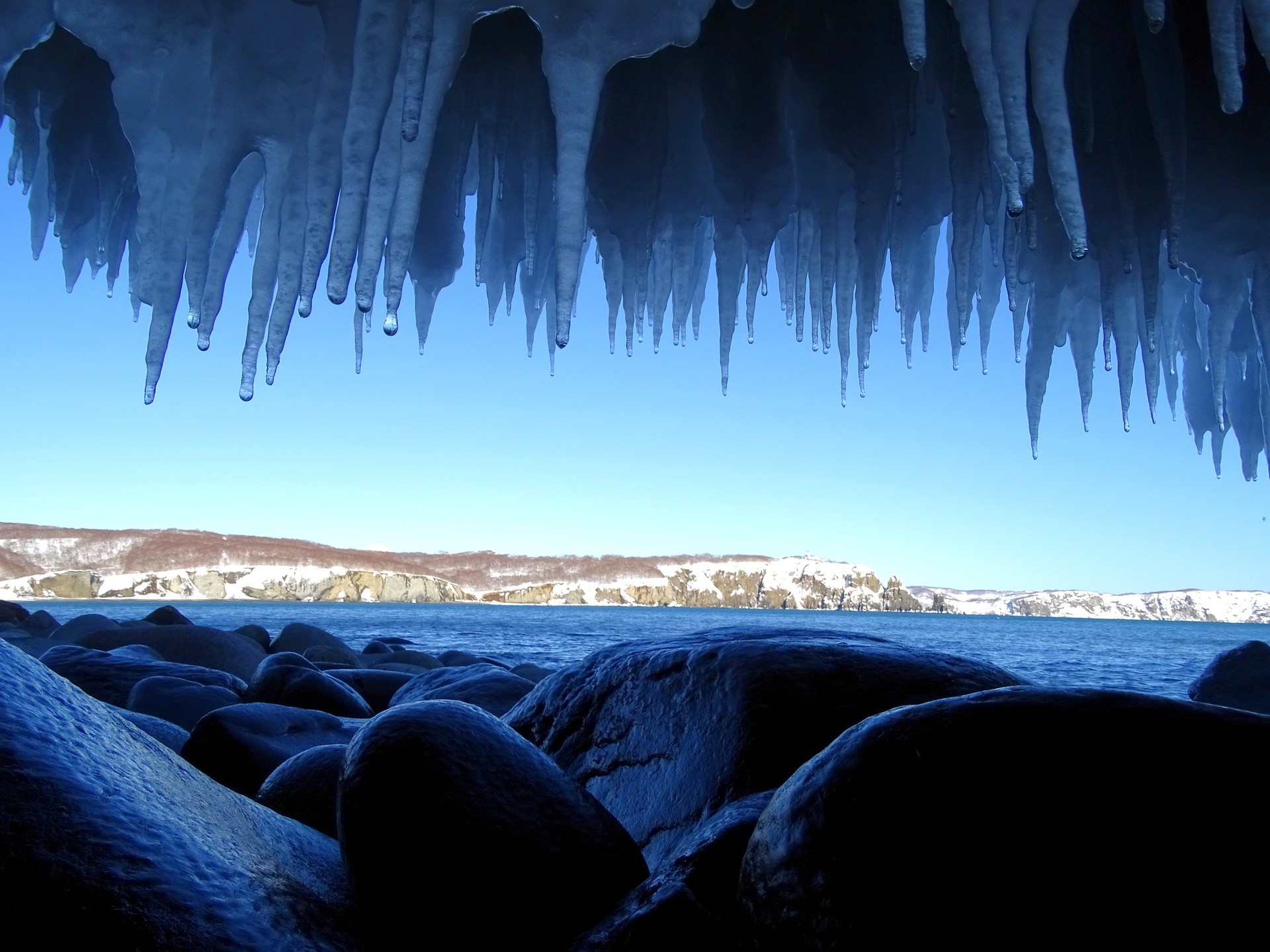 Icicles hanging over a rocky shore and the sea HD Wallpaper
