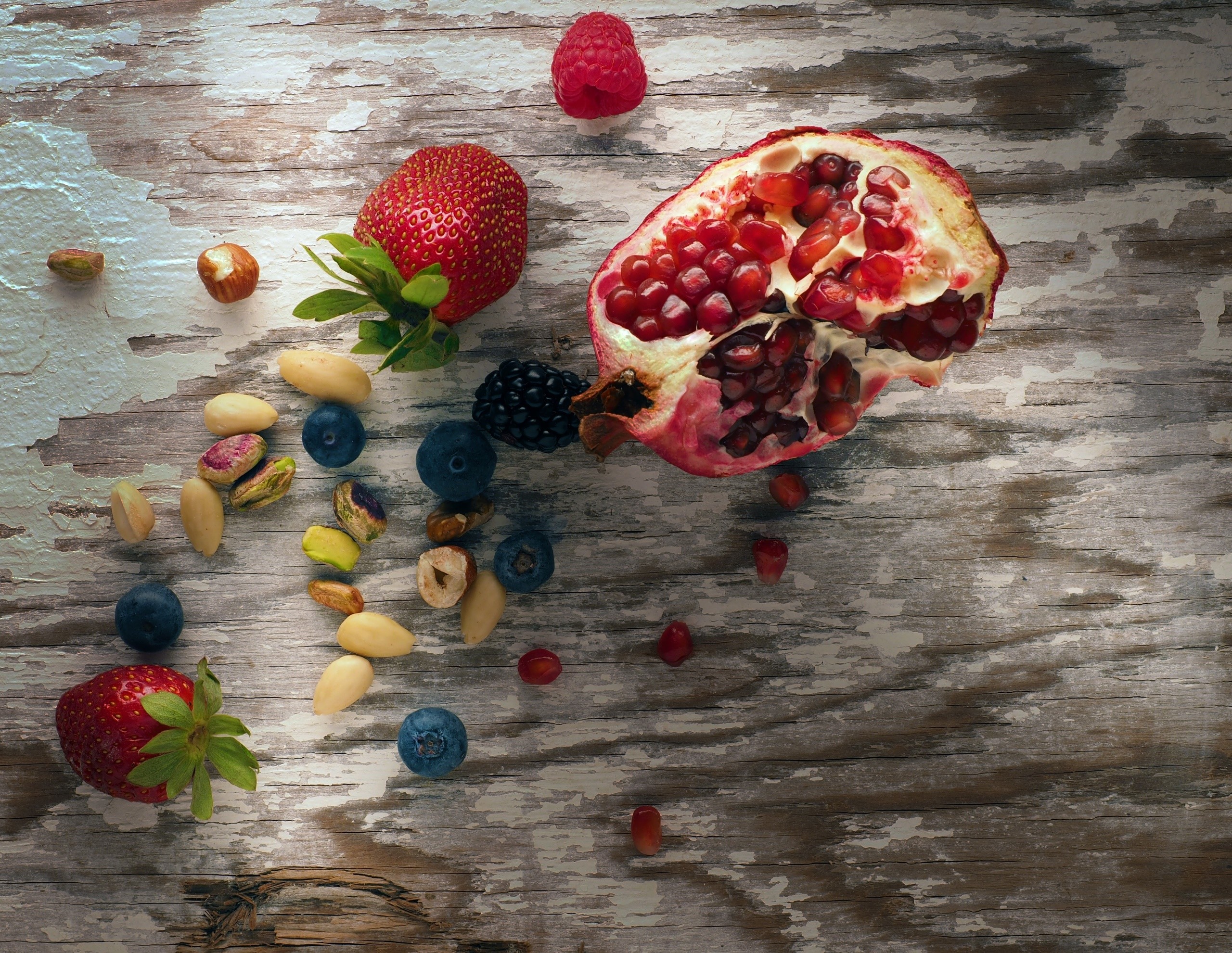Pomegranate, berries, and nuts on a wooden surface HD Wallpaper