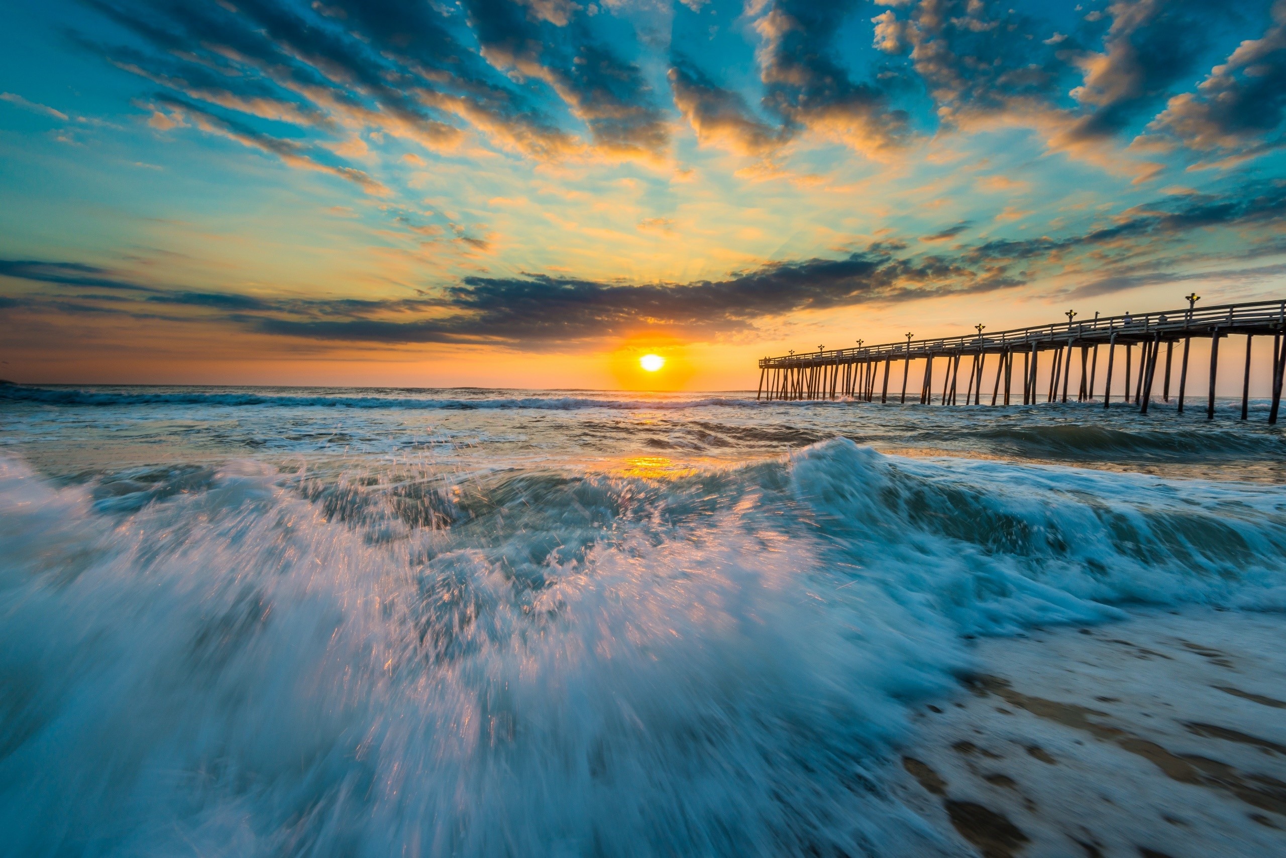 Sunrise over the ocean with a pier and waves HD Wallpaper