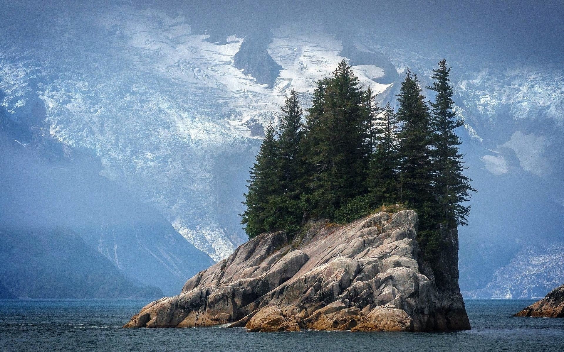 Rocky island with pine trees and snowy mountains HD Wallpaper