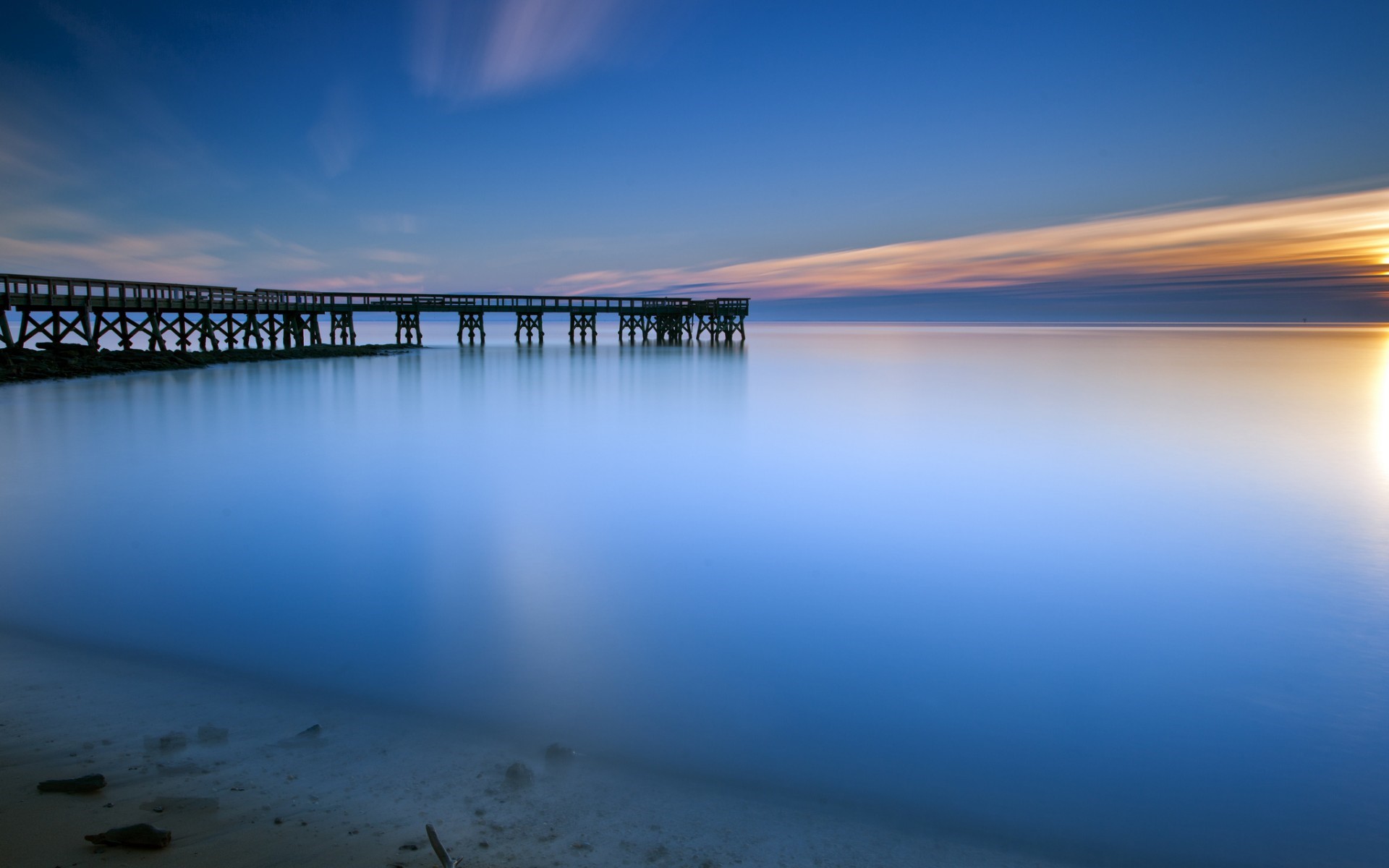 Long exposure of a pier at sunset over calm water HD Wallpaper