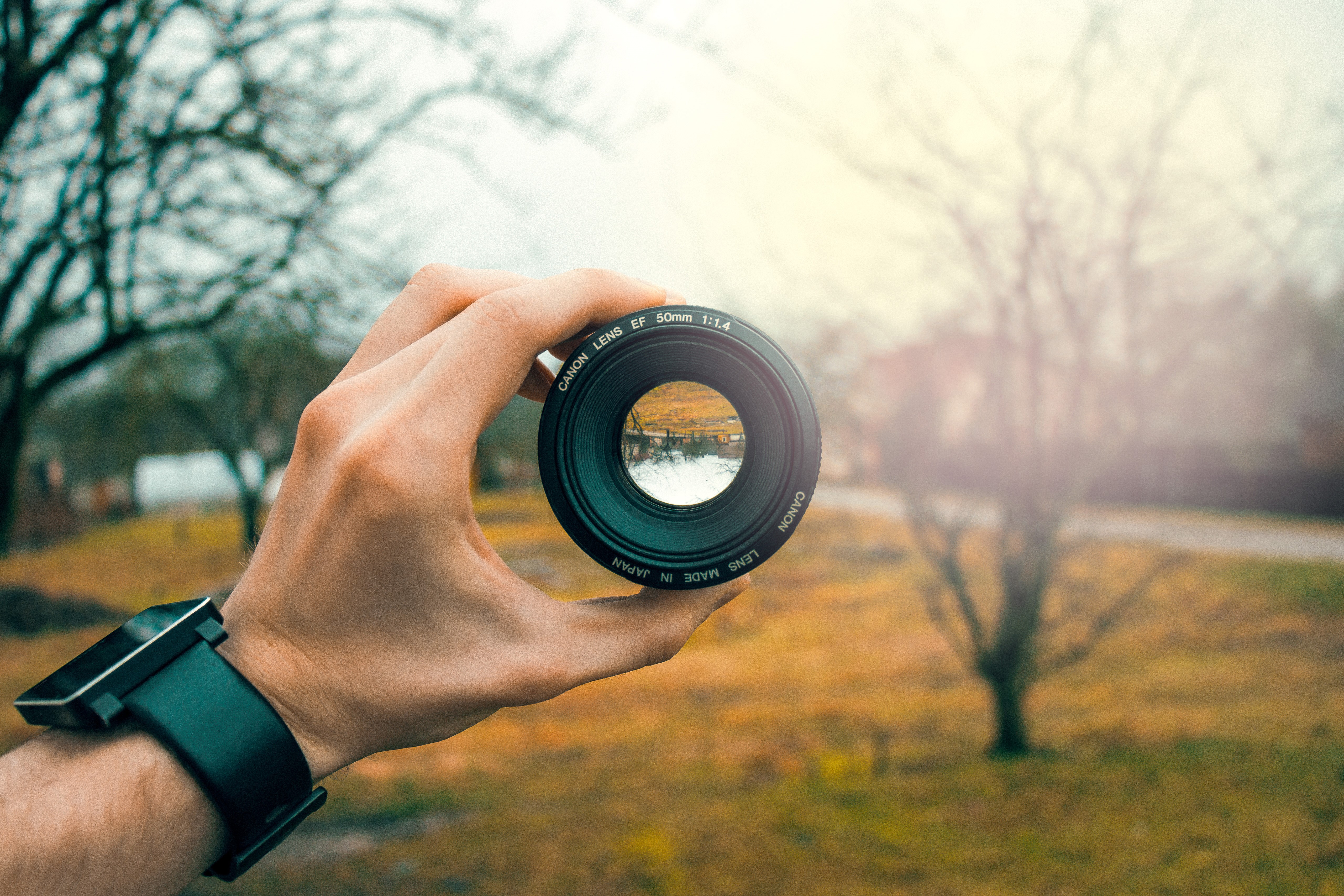 Hand holding Canon camera lens with nature view HD Wallpaper