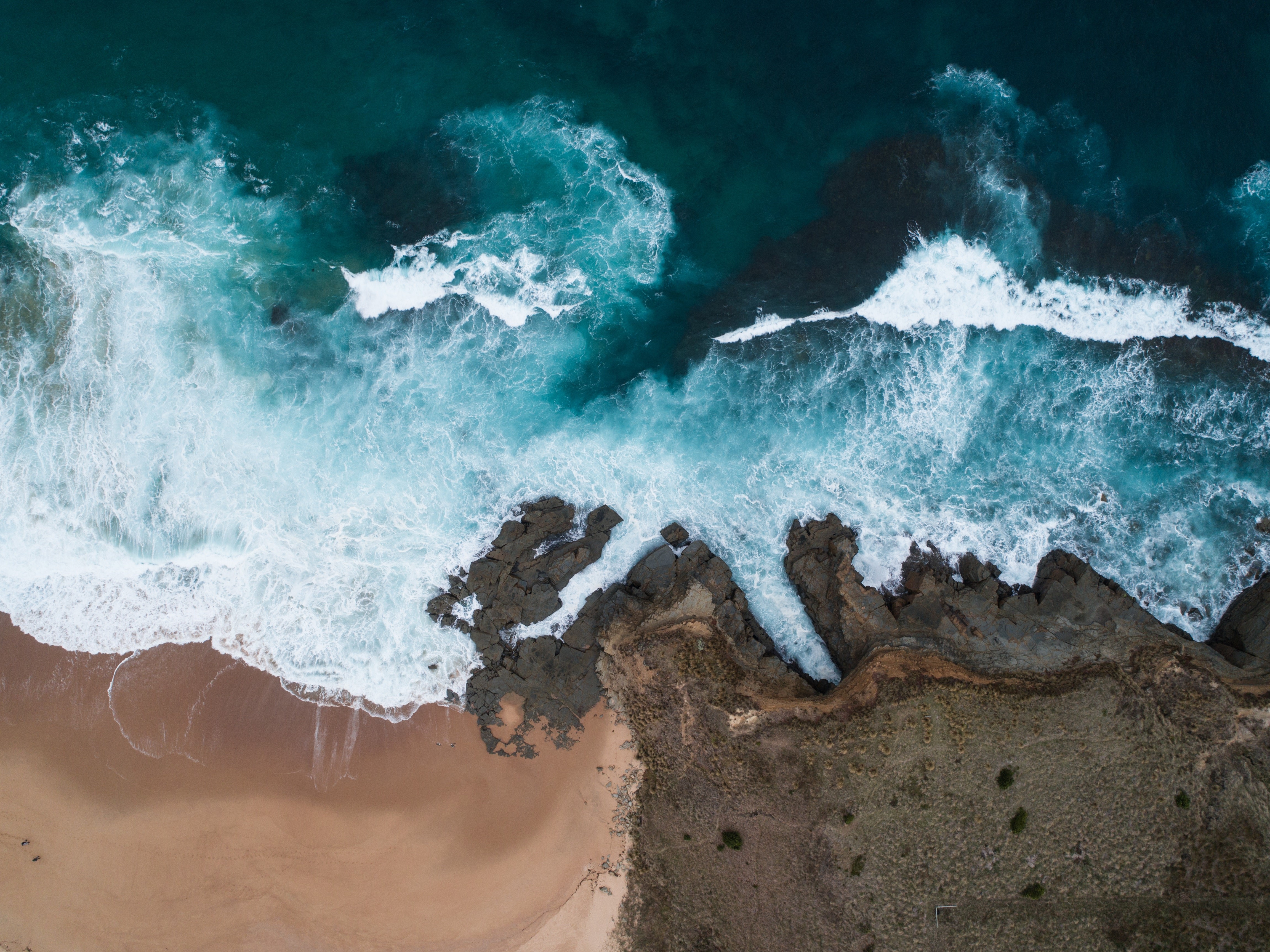 Aerial view of ocean waves crashing on a rocky beach HD Wallpaper