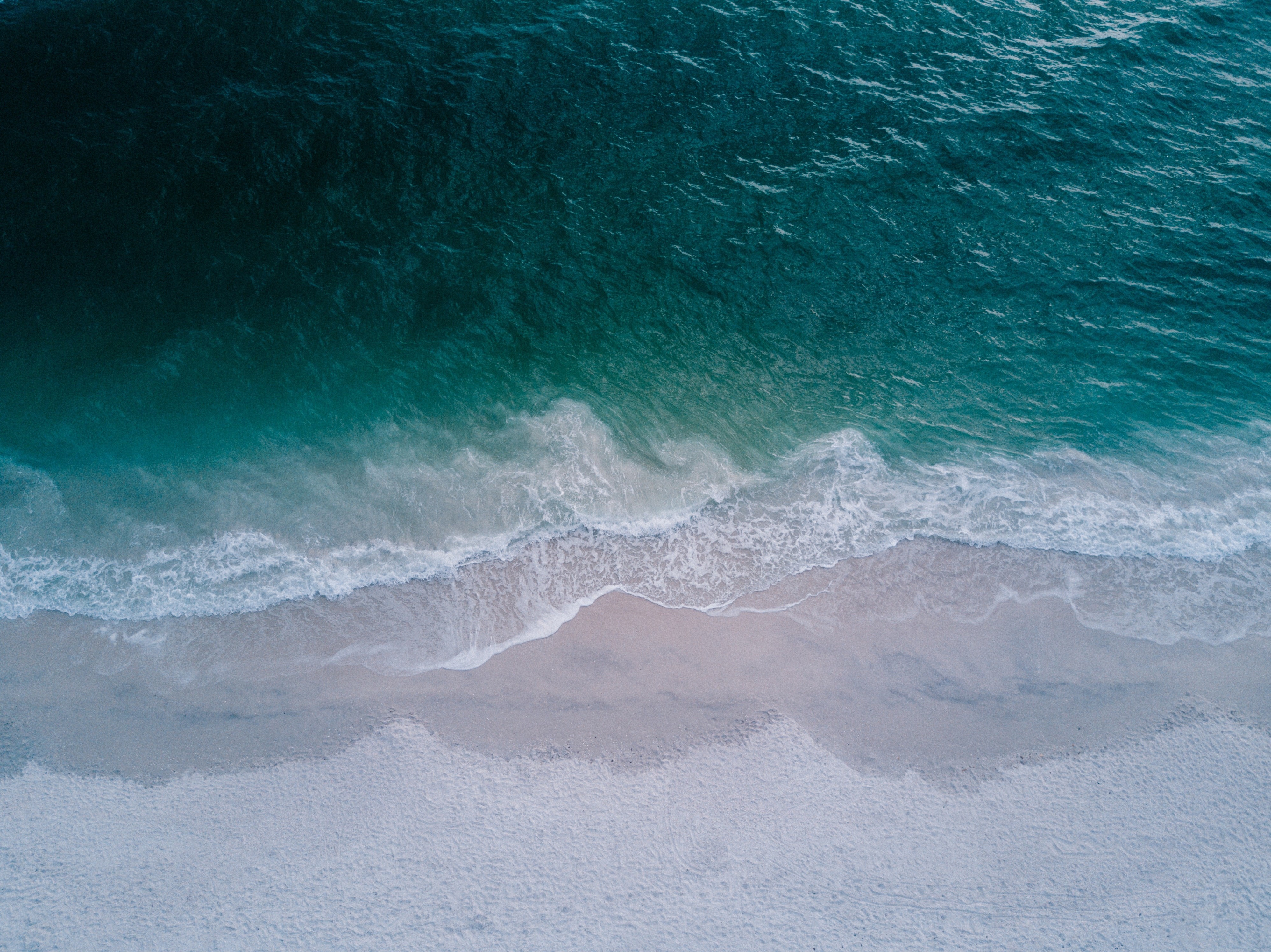 Aerial view of ocean waves crashing on a sandy beach HD Wallpaper