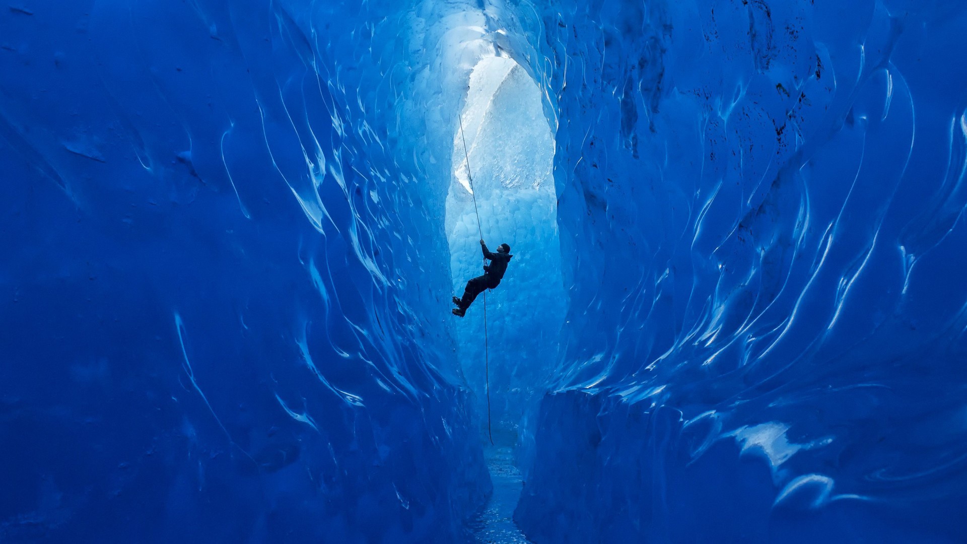 Person rappelling down a blue ice cave HD Wallpaper