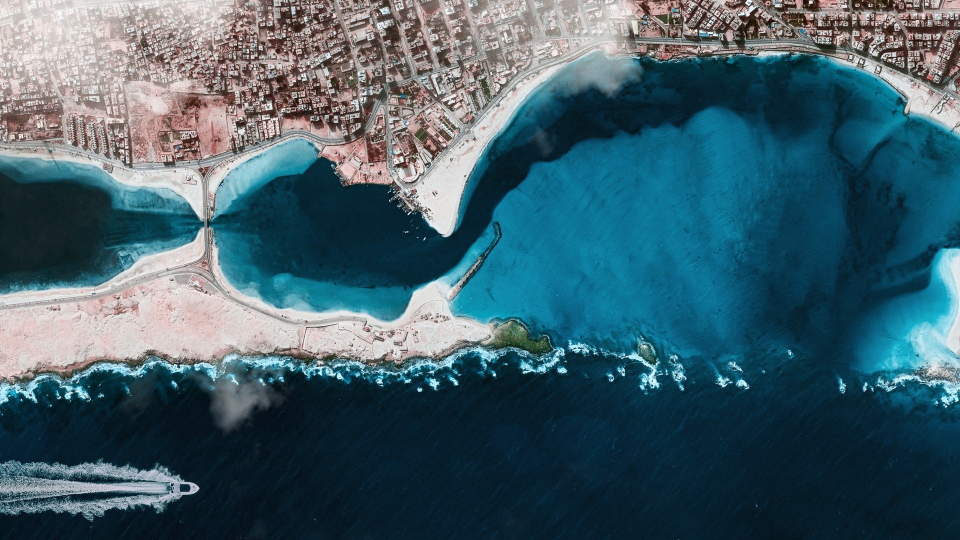 Aerial view of a coastal city with a bay and a boat HD Wallpaper