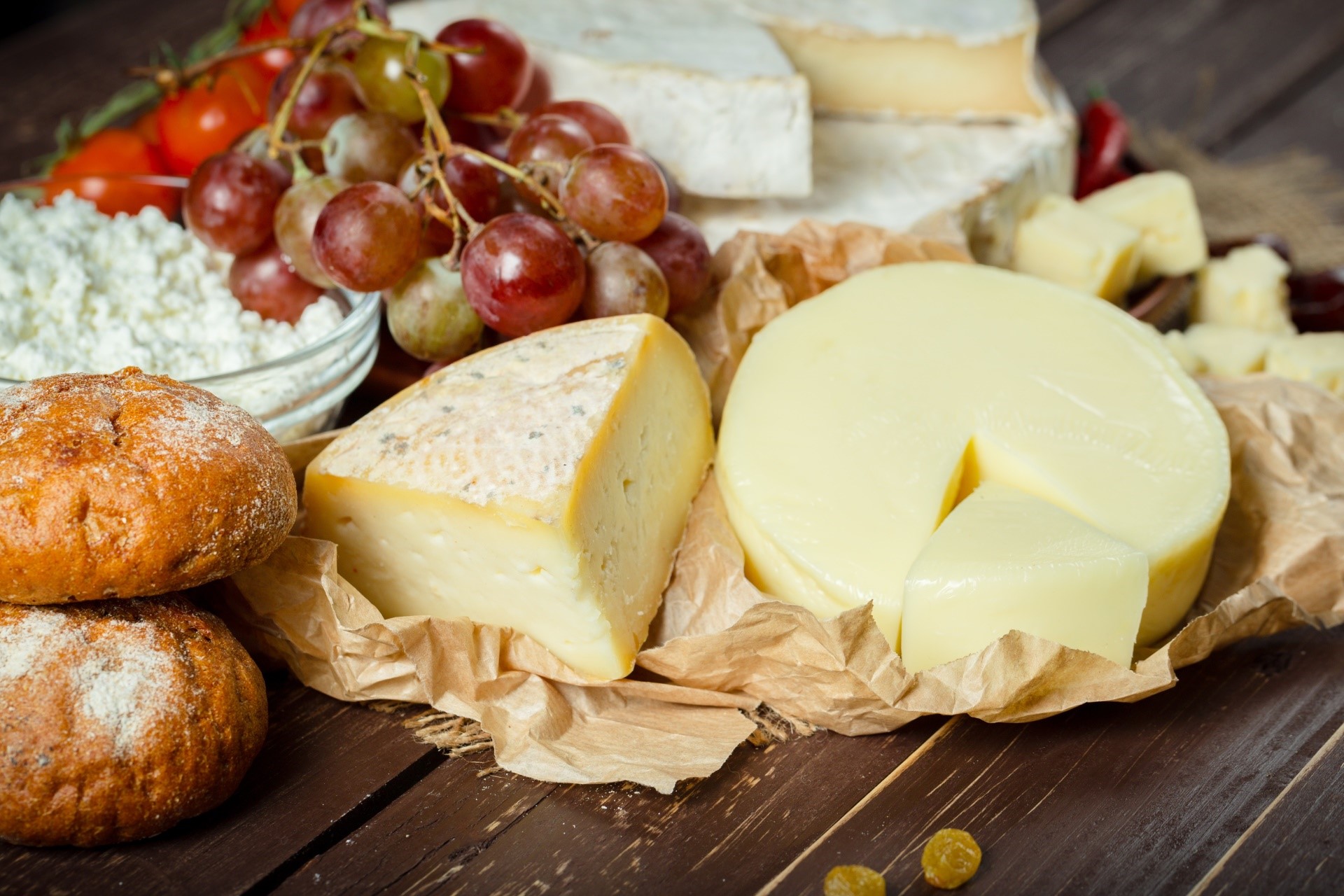 Cheese, bread, grapes, and tomatoes on a wooden table HD Wallpaper