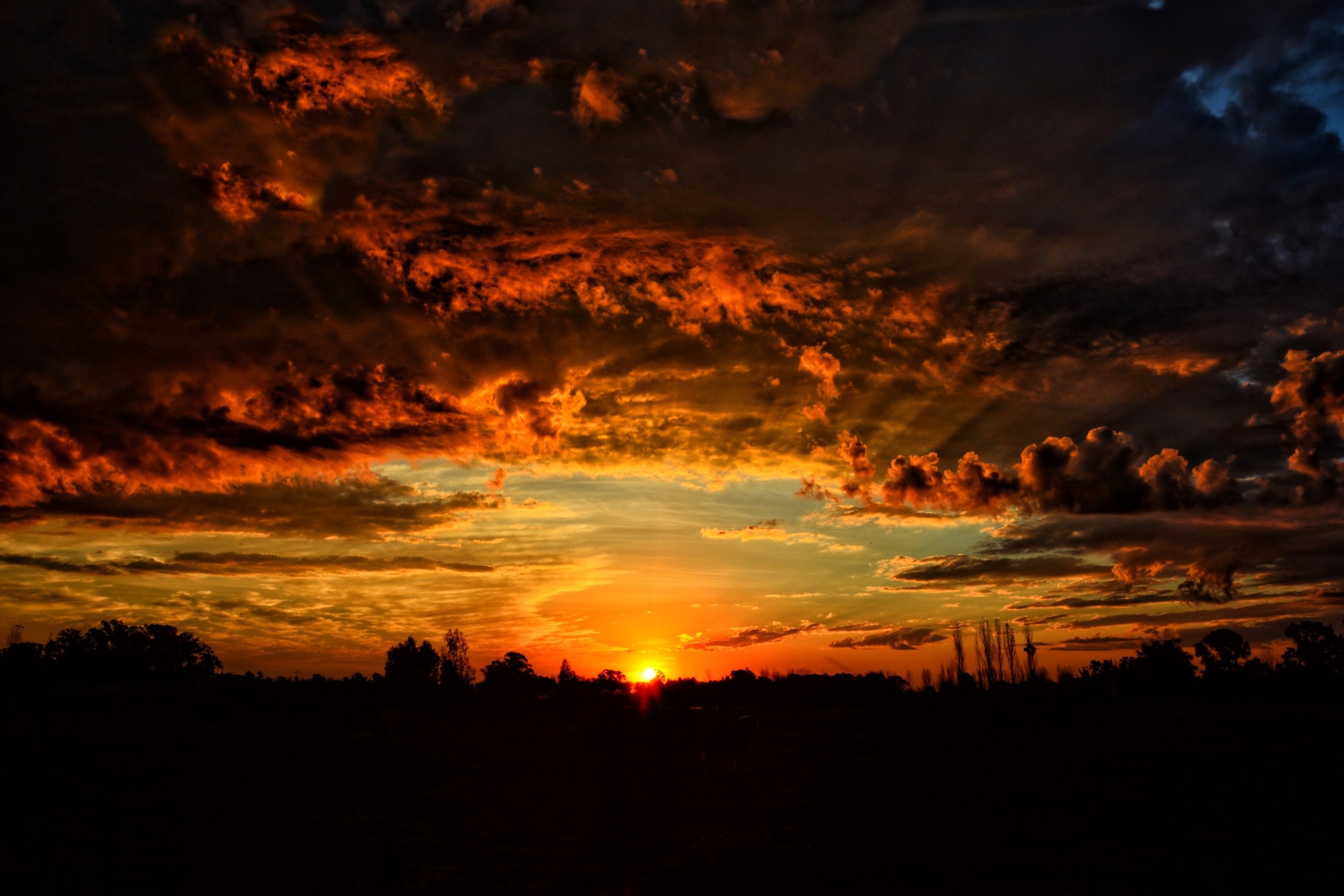 Dramatic sunset with fiery clouds over silhouetted landscape HD Wallpaper