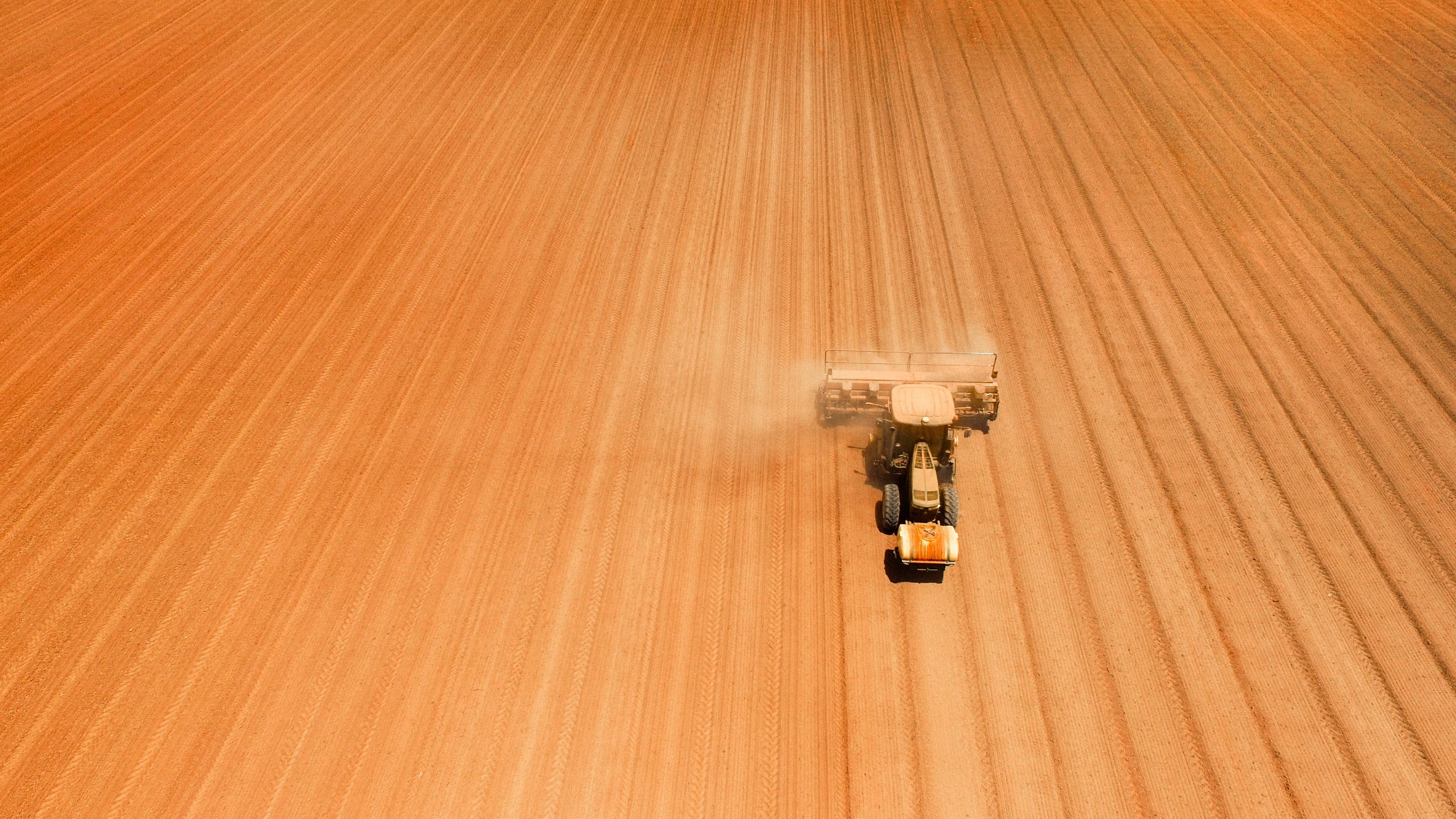 Tractor plowing a dusty field from an aerial view HD Wallpaper