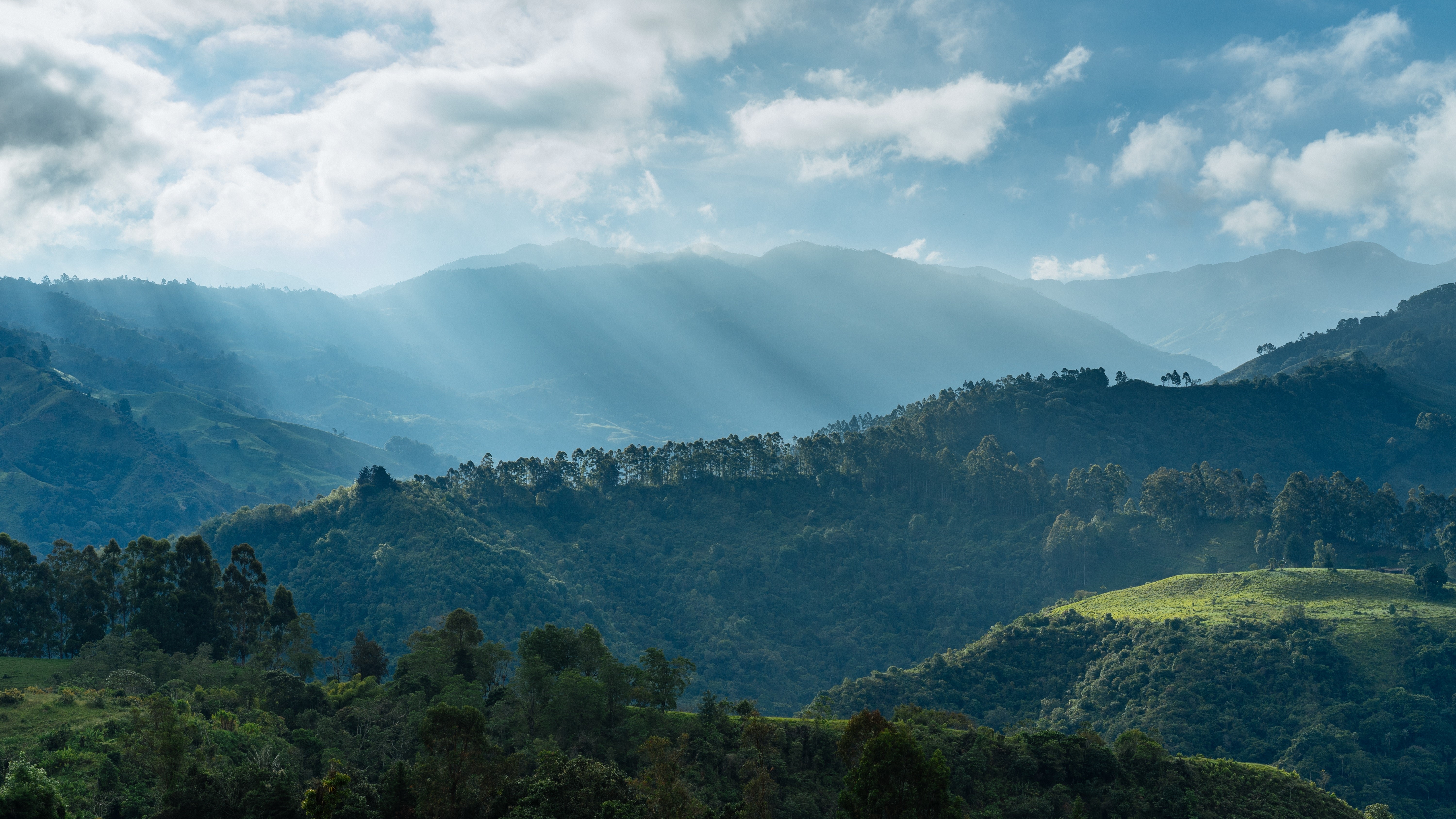Sunlight beams through clouds over Colombian mountains and forests HD Wallpaper