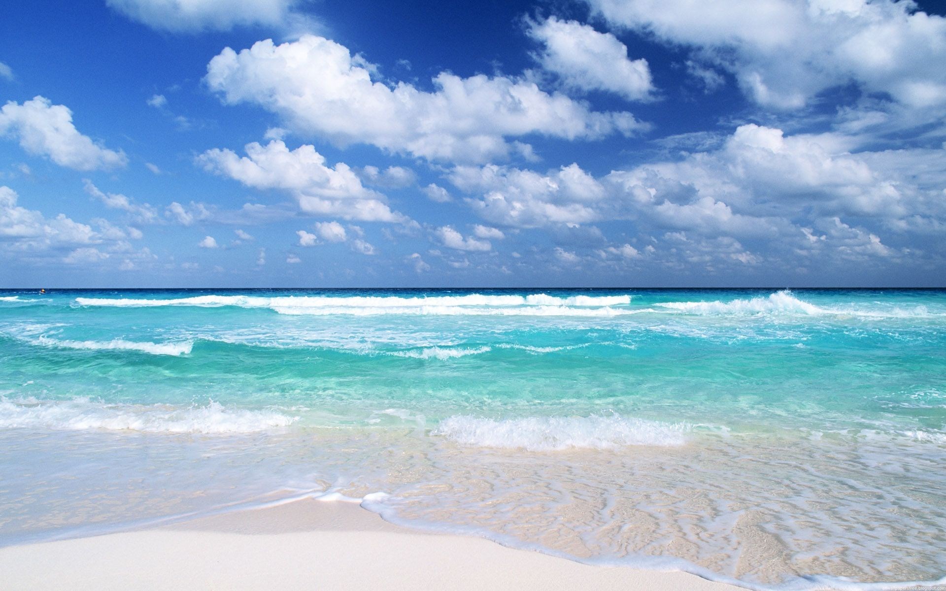 Turquoise ocean waves crash on a white sand beach under a blue sky with clouds. HD Wallpaper