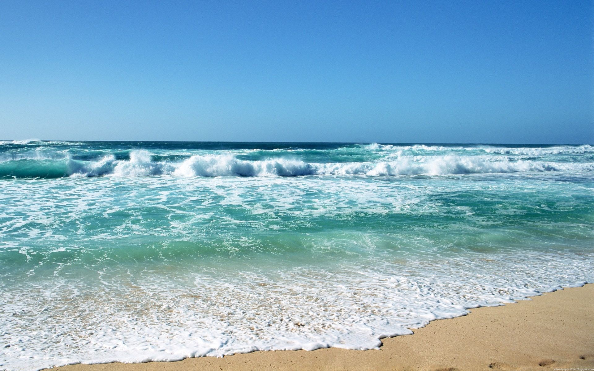 Ocean waves crashing on a sandy beach under a clear blue sky HD Wallpaper